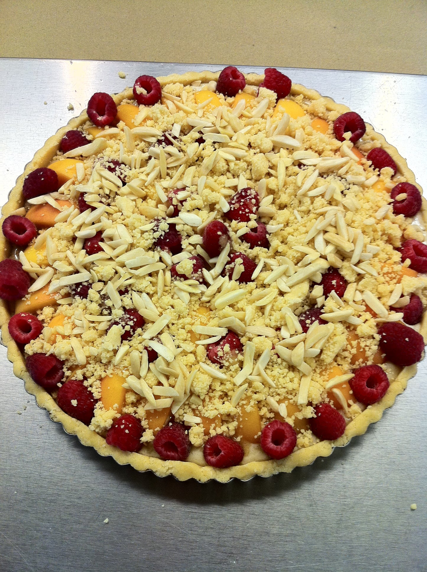 Unbaked tart with fruit and crumb topping on a metal surface