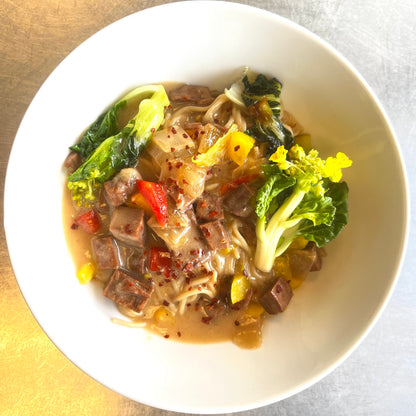 A bowl of vegan Filipino adobo with braised soy and pea-based chicken, served with vegetable garnish and Asian rice.