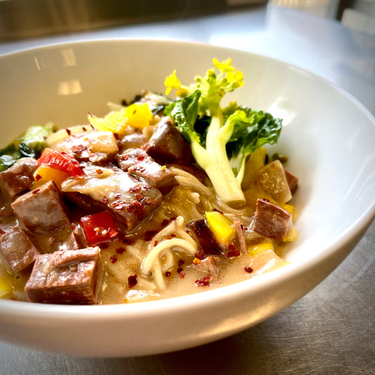 A bowl of vegan Filipino adobo with braised soy and pea-based chicken, served with vegetable garnish and Asian rice.