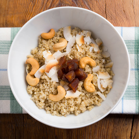 Quinoa breakfast bowl with coconut milk, dried fruit, and toasted nuts in a white ceramic bowl