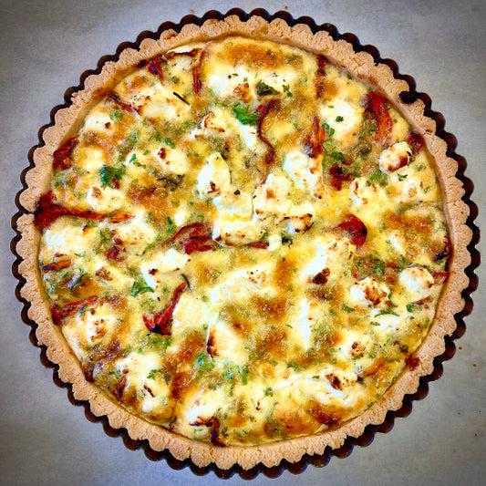 A roasted tomato and goat cheese tart in a pastry crust, topped with herbs and cheese, with a side green salad and dressing.