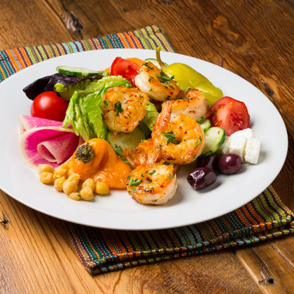 A plate of Greek Grilled Shrimp Salad with grilled shrimp, fresh vegetables, olives, feta cheese, and a red wine vinaigrette dressing.
