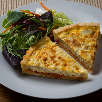 Two slices of Artichoke & Sun Dried Tomato Tart with a side green salad and dressing on a white plate.